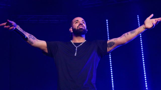 drake giving stage performance wearing a black tshirt and tattos on wrist and arms and a mic in right hand